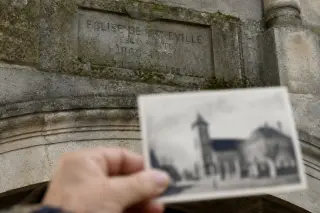 Moss-covered inscription on the church façade, soft morning light, archival photo held in blurred foreground, conveying a quiet historical comparison.